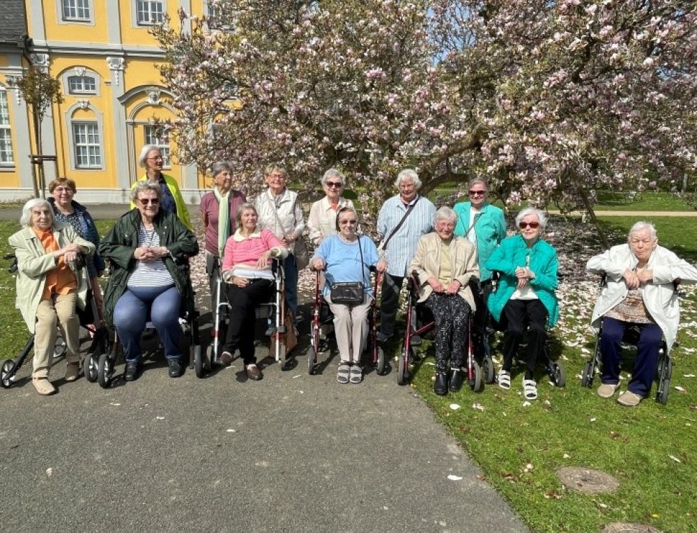 Senior*innen sitzen und stehe nebeneinander und schauen freudig in die Kamera 