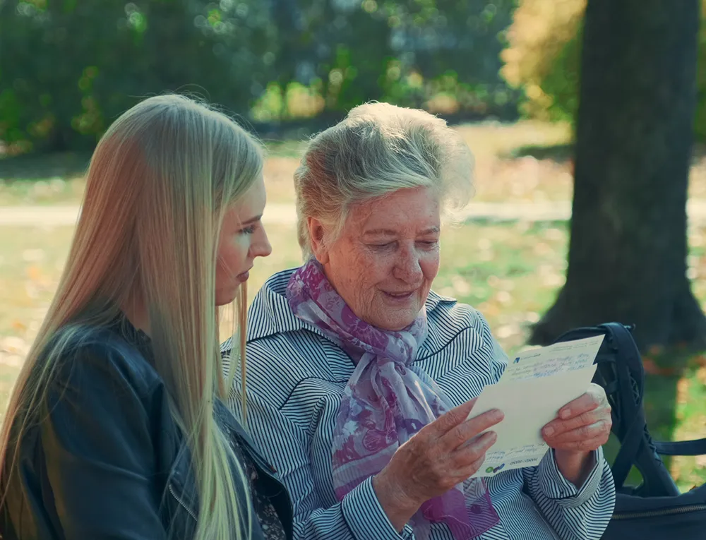 Eine ältere Dame sitzt mit einer jungen Frau zusammen auf einer Parkbank.
